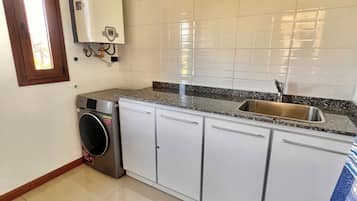 Una cocina con armarios blancos, un lavamanos de acero inoxidable, lavadora incorporada y una ventana con vistas.