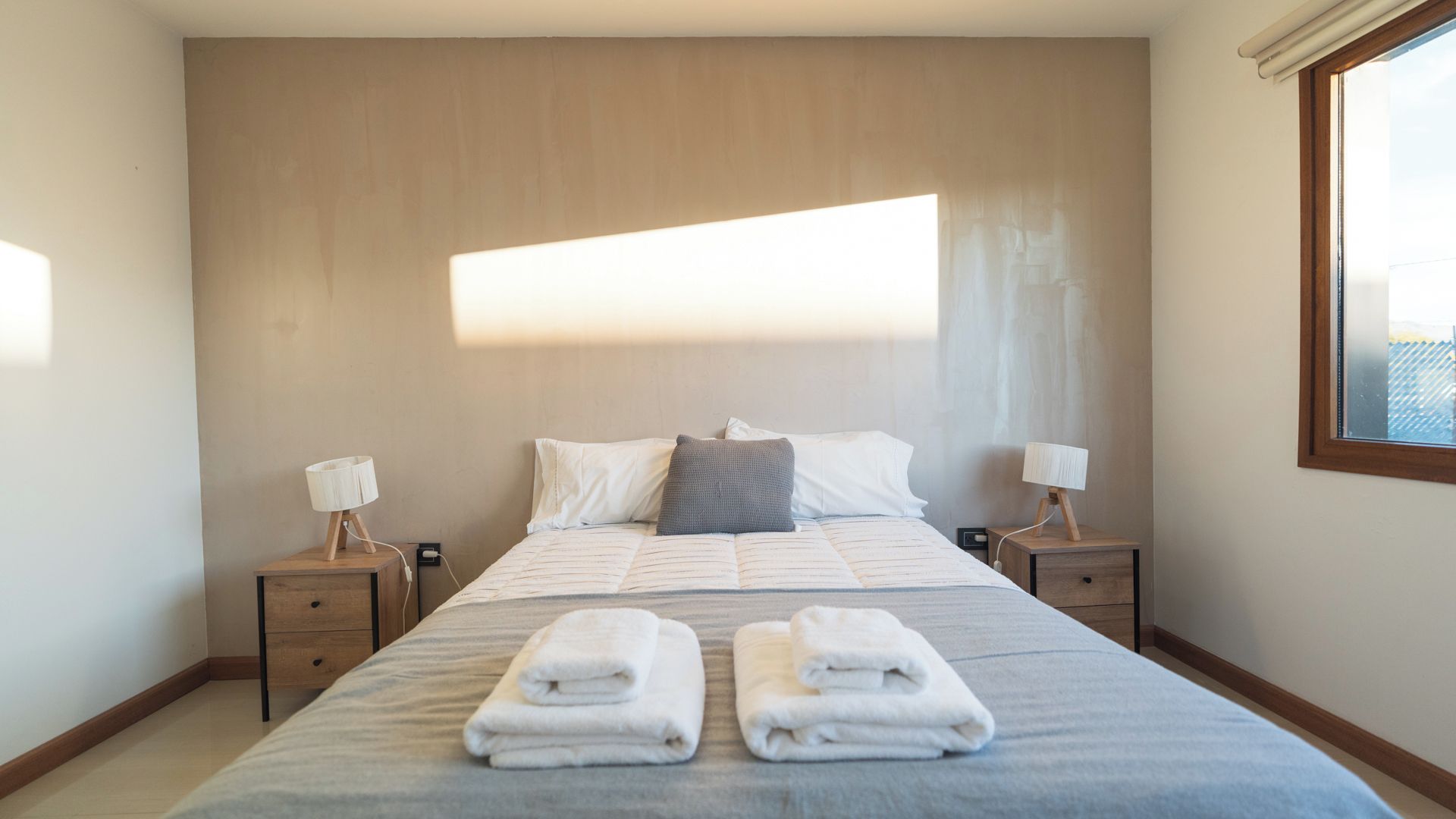 A hotel room with a large bed, two bedside tables with lamps, a window, and a view of the sky.