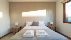A hotel room with a large bed, two bedside tables with lamps, a window, and a view of the sky.