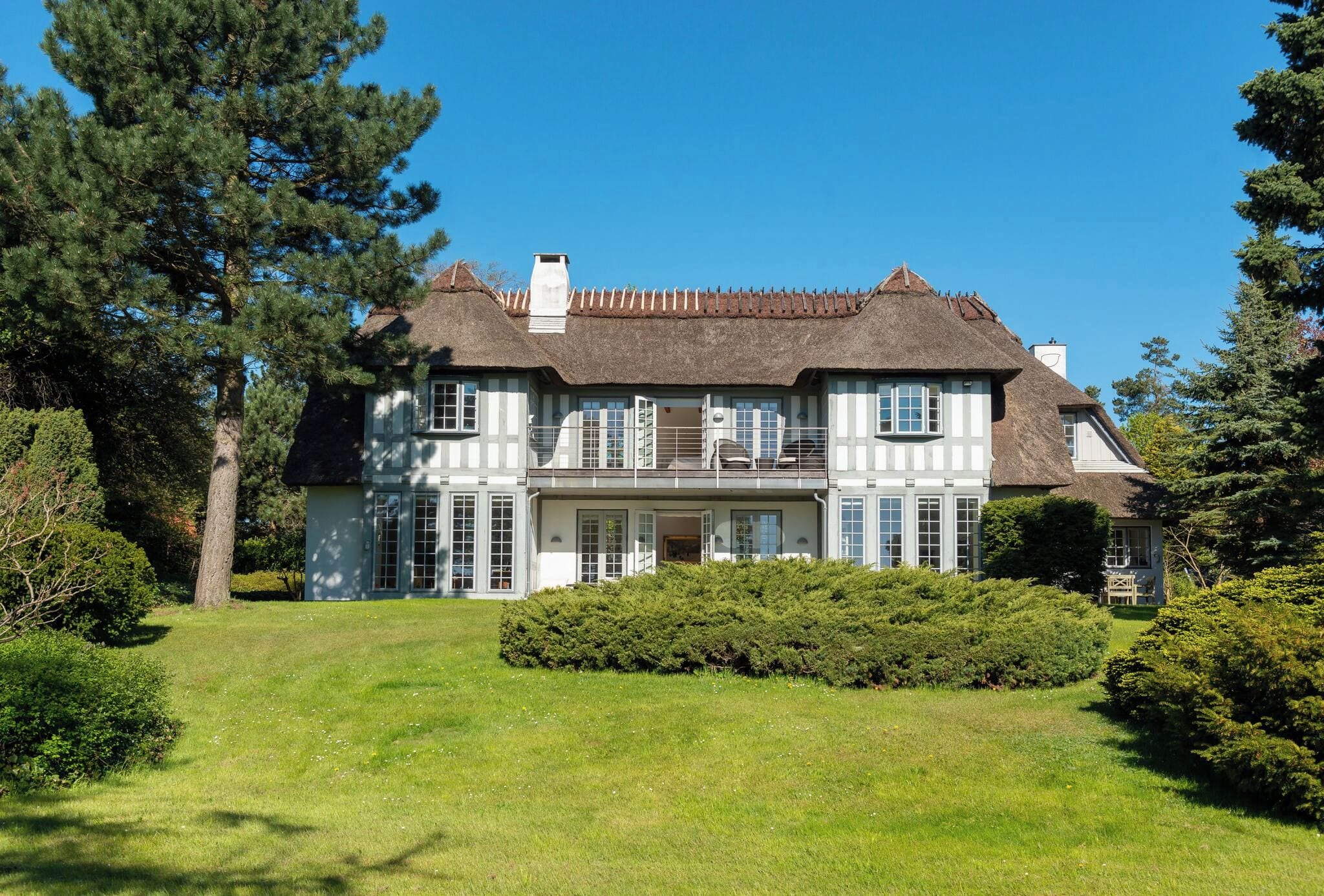 A large, two-story house with a thatched roof, surrounded by a well-maintained lawn and dense trees.