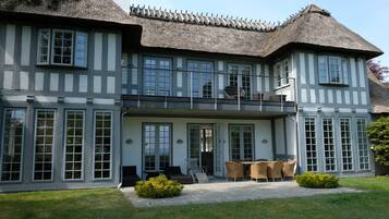 A two-story house with a thatched roof, large windows, and a balcony with outdoor furniture.