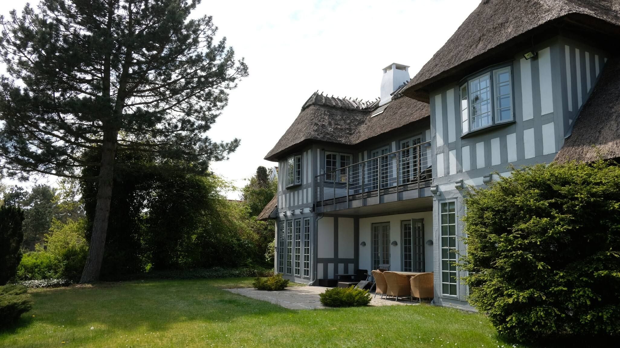 A two-story house with a thatched roof, a balcony, and a well-maintained garden.