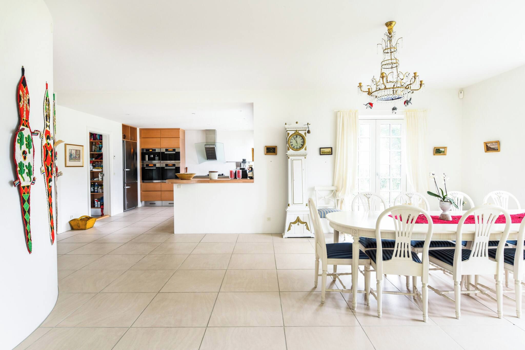 Una cocina amplia con electrodomésticos modernos, un comedor con candelabro y un reloj grande en la pared.