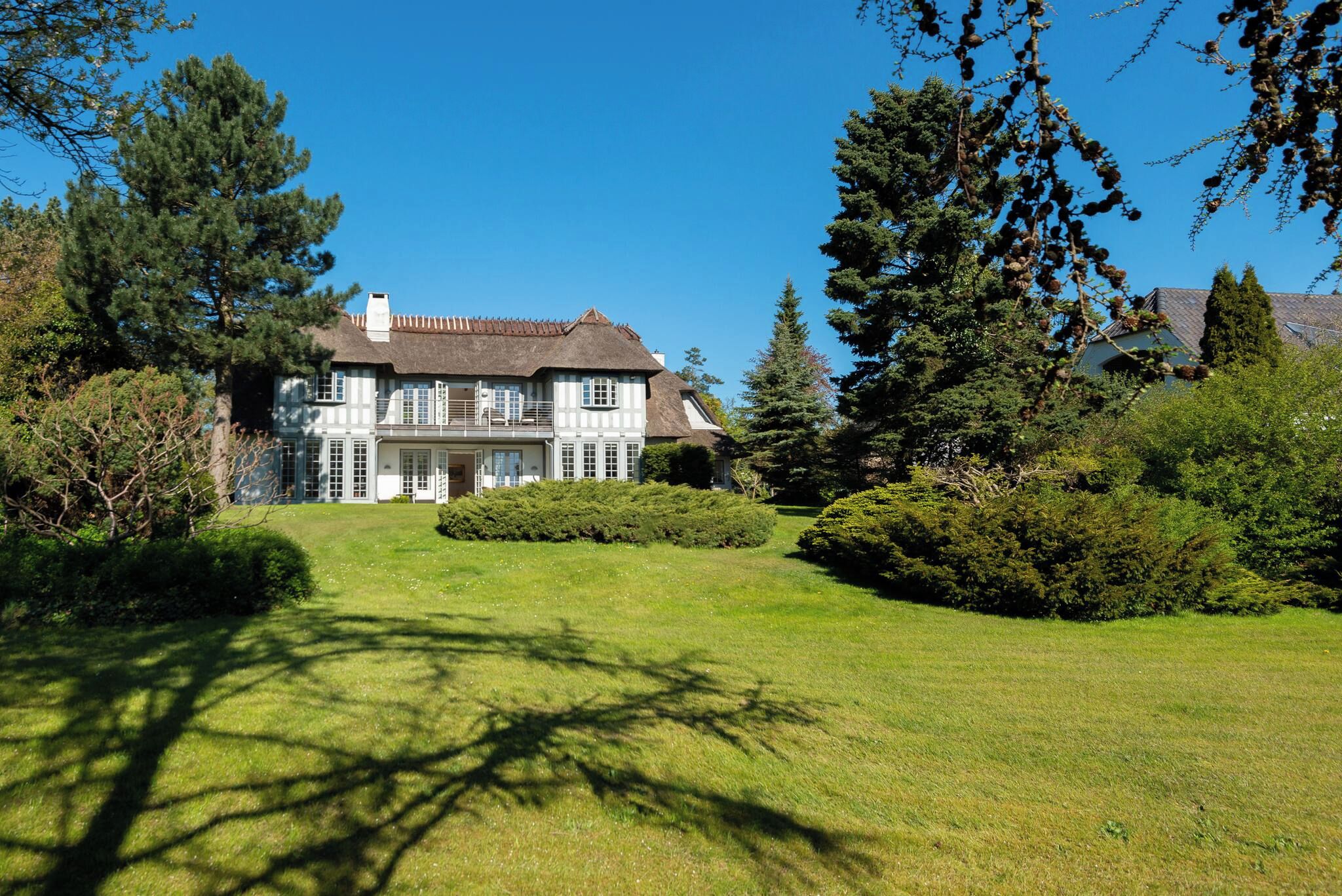 A large house with a thatched roof, surrounded by a well-maintained lawn and dense trees.