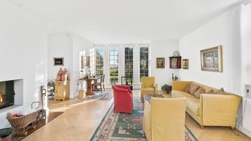 A spacious living room with a fireplace, a yellow sofa, a red chair, and a large window with a view of greenery.
