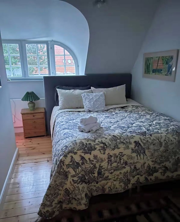 Un dormitorio con cama, mesita de noche, lámpara y ventana.