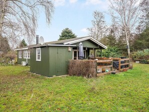 A green wooden house with a porch, a satellite dish, and a small garden area. - 4 Star Holiday Home in Idestrup (Idestrup)
