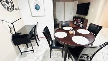 A dining area with a round table, black chairs, a clock, and a framed artwork on the wall.