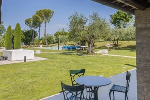 A patio area with a round table and two chairs, a swimming pool, and a garden with trees and a hammock. - VILLA ANNA: HEATED POOL, 2 OUTDOOR HOT TUBS, SAUNA, AND GYM (Sant'Ippolito)
