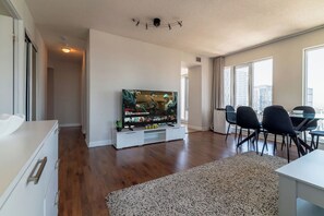 Ein modernes Wohnzimmer mit Flachbildfernseher, einem Essbereich mit Stühlen und einem großen Fenster mit Blick auf die Stadt.
