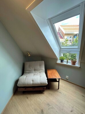 Ein Schlafzimmer im Loft-Stil mit schrägem Dach, einem Bett, einem Schreibtisch und einem Fenster mit Pflanzen.