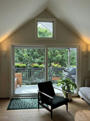 Ein Zimmer mit hoher Decke, einer Schiebetür zum Balkon, einem Sessel, einer Topfpflanze und einem kleinen Tisch.
