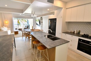 A modern kitchen with a central island, bar stools, a built-in oven, and a large window. - Villa 33 - Tangalooma - Moreton Island (moreton island)