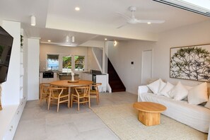 A modern living room with a dining area, a staircase, and a kitchen with large windows. - Villa 33 - Tangalooma - Moreton Island (moreton island)