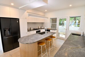 A modern kitchen with a built-in island, stainless steel appliances, and a large window providing a view of the outdoors. - Villa 33 - Tangalooma - Moreton Island (moreton island)
