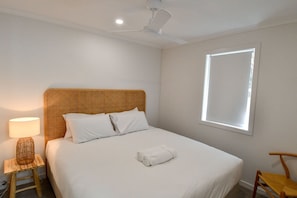 A bedroom with a bed, a bedside lamp, a window, and a ceiling fan. - Villa 33 - Tangalooma - Moreton Island (moreton island)