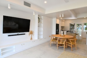 A modern living room with a flat-screen TV, a dining area with wooden chairs, and a kitchen with a large island. - Villa 33 - Tangalooma - Moreton Island (moreton island)