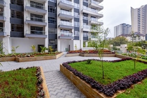 A modern apartment building with multiple balconies, a landscaped courtyard with grass and plants, and a paved walkway. - Chic 2BR with HeatedPool, Gym, Sauna, SteamRoom, Wi-fi , Safe Parking (Nairobi)