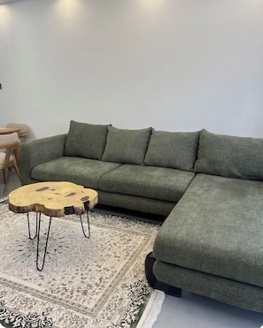 A green sectional sofa with a round wooden coffee table with metal legs. - Chic 2BR with HeatedPool, Gym, Sauna, SteamRoom, Wi-fi , Safe Parking (Nairobi)