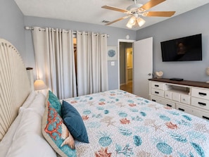 Ein Schlafzimmer mit Bett, Deckenventilator, Fernseher und Kommode.