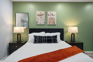 Une chambre d’hôtel comprenant un lit, deux tables de chevet, deux lampes fixées au mur et deux tableaux encadr és au-dessus du lit.