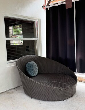 Une chaise en osier avec un coussin, placée devant une fenêtre munie de stores.