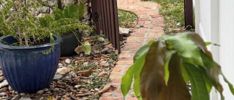 A garden pathway with a brick floor, surrounded by potted plants and a stone wall.
