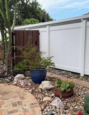 A garden area with a brick pathway, a potted plant, a cactus, and a white fence. - Cozy Private entrance 1-bedroom in charming  2 Miles Away from Sunny Isles Beach (North Miami Beach)