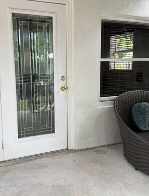 A white door with a metal security grill, a window with blinds, and a wicker chair with a cushion. - Cozy Private entrance 1-bedroom in charming  2 Miles Away from Sunny Isles Beach (North Miami Beach)