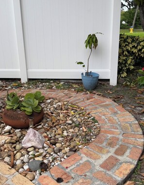 Un chemin circulaire pavé de briques, bordé d’un petit espace jardin où se trouvent une plante succulente et une plante en pot.