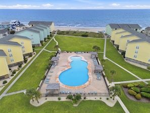 Un resort con piscina central, varias zonas de descanso y vistas al océano.