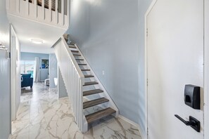 Eine Treppe mit weißen Geländern führt zu einer Zwischenebene, einer Tür mit schwarzem Griff und einem Blick in einen Raum mit blauer Wand und einem Gemälde.