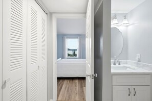 Quarto com cama, janela com cortinas, banheiro com pia e espelho e corredor com armário.