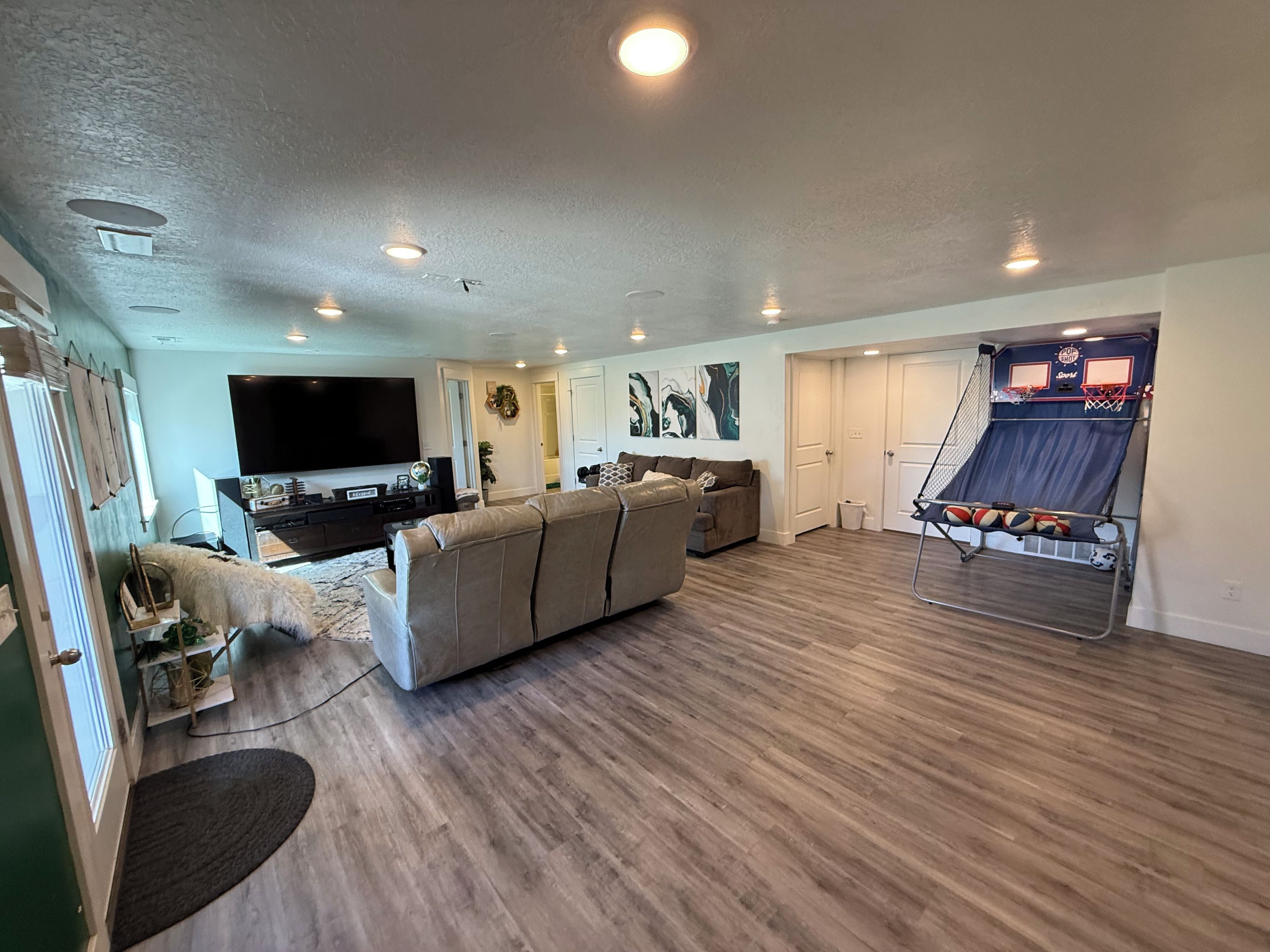 A living room with a large flat-screen TV, a beige sectional sofa, and a basketball hoop.