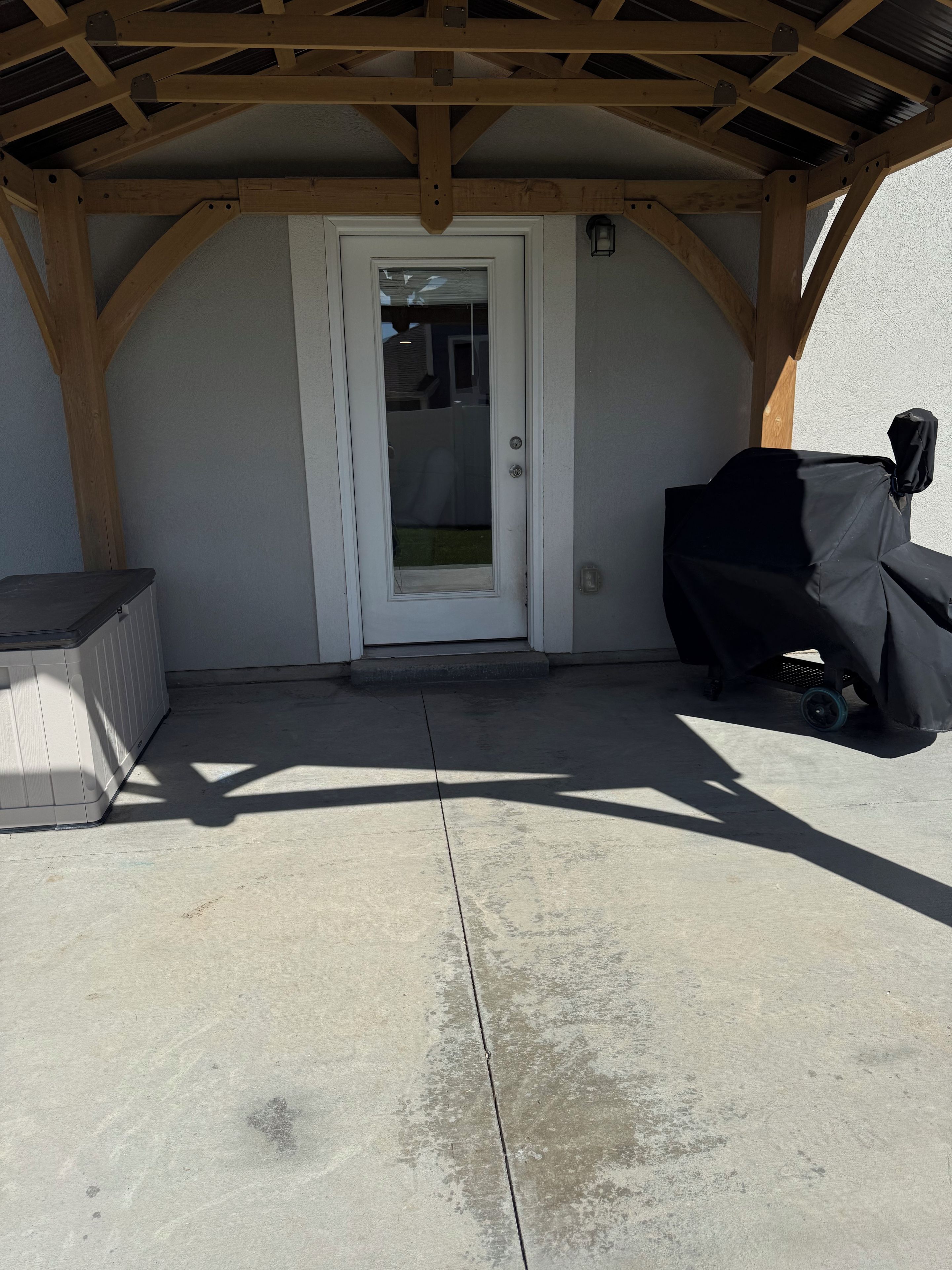 A covered patio area with a white door, a barbecue grill, and a concrete floor.