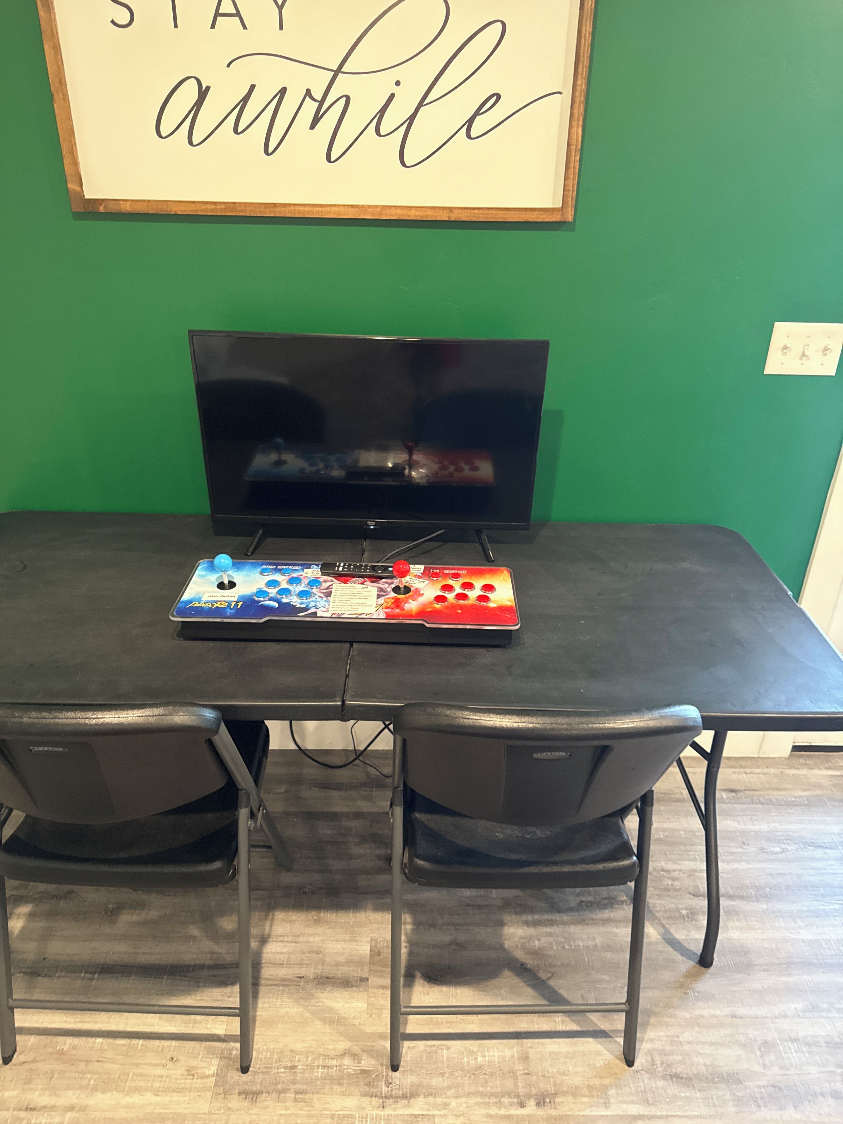 A dining table with a video game console, two chairs, and a framed sign on the wall.
