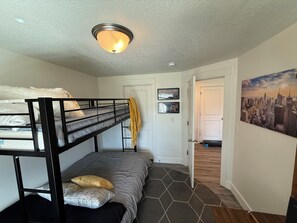 Una habitación con literas, una cama individual, una puerta que da a otra habitación y un cuadro de un paisaje urbano en la pared.