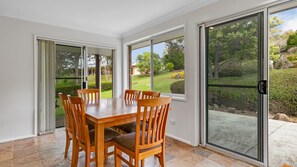 A dining area with a wooden table and chairs, large sliding glass doors, and a view of a landscaped garden. - Bawley Point Coastal Acreage - Guest Retreat (Bawley Point)