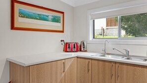 Una cocina con encimera blanca, armarios de madera, pileta de acero inoxidable, un tostador y un cuadro en la pared.