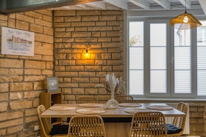 A dining area with a brick wall, a table with woven placemats, wicker chairs, and a hanging light fixture. - L'Ecrin de Maysel - Nature & Comfort (Maysel)