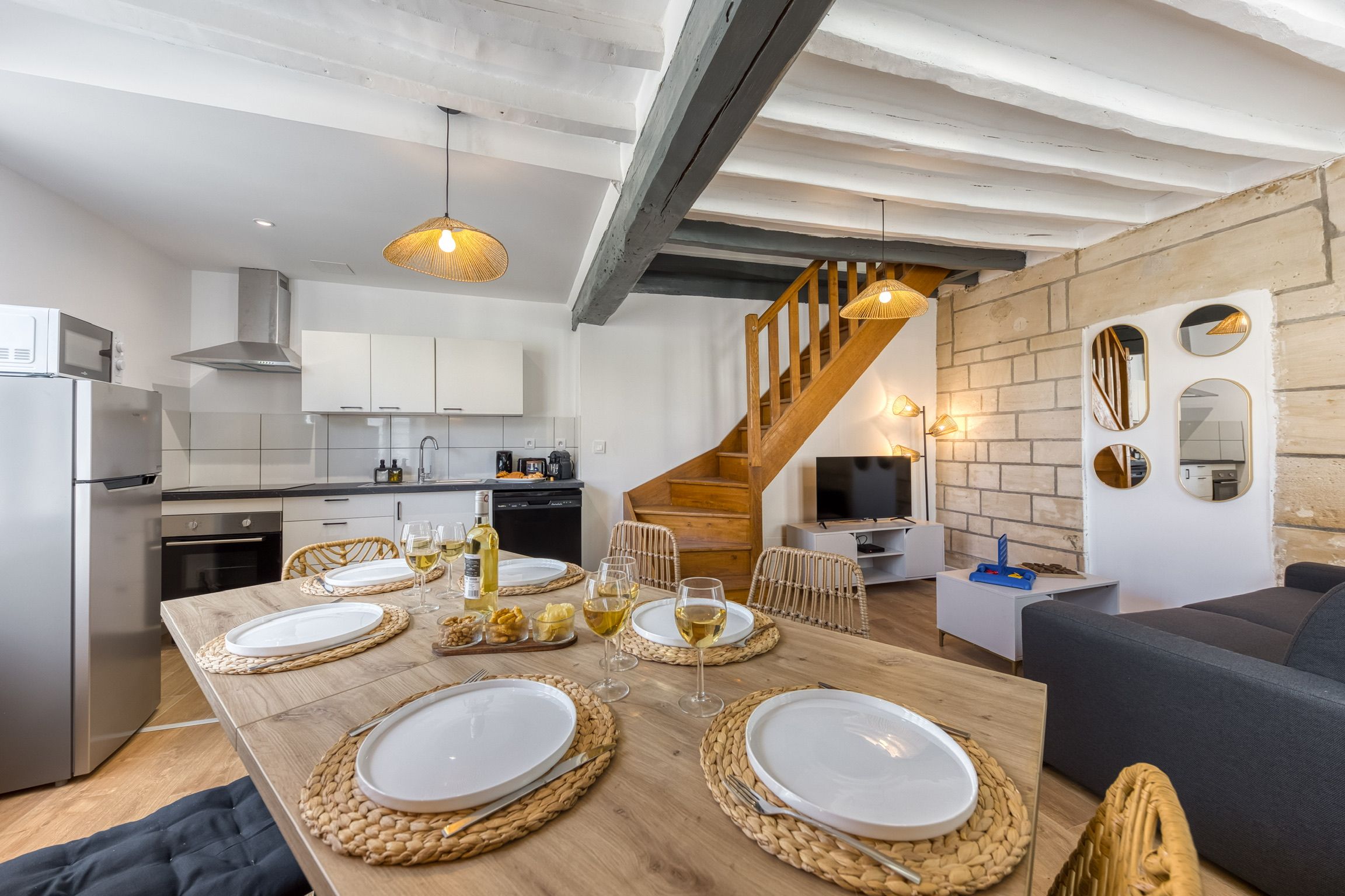 Eine moderne Küche mit weißen Schränken, einem Holzespeisetisch, gedeckt für vier Personen, und einer Treppe, die zu einem Erker führt.