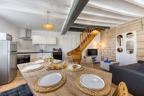 A modern kitchen with white cabinets, a wooden dining table set for four, and a staircase leading to a loft area. - L'Ecrin de Maysel - Nature & Comfort (Maysel)