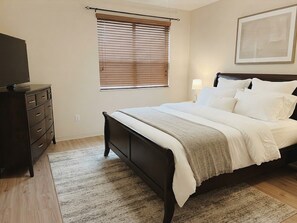 A bedroom with a bed, a dresser, a window with blinds, a lamp, and a framed picture on the wall. - Modern Palm Coast Oasis with Private Pool (Palm Coast)