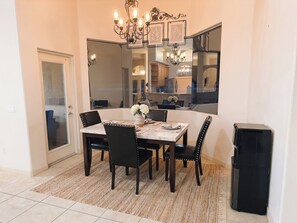 A dining area with a table set for four, surrounded by chairs, a rug, and a large mirror reflecting the kitchen. - Modern Palm Coast Oasis with Private Pool (Palm Coast)