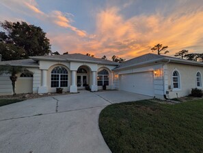 A two-story house with a driveway leading to a garage, surrounded by a well-maintained lawn and trees. - Modern Palm Coast Oasis with Private Pool (Palm Coast)