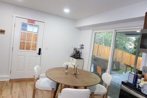A dining area with a round table, four chairs, a coffee machine, and a view of a wooden deck through a sliding glass door. - Peaceful 5-bedroom house with AC in beautiful Lynnwood (Lynnwood)