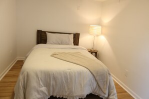 Ein schmales Zimmer mit einem Einzelbett, einer Nachttischlampe und Holzboden.