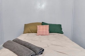Ein Bett mit gesteppter Bettdecke, zwei zusammengerollte Handtücher und drei Kissen in verschiedenen Farben.