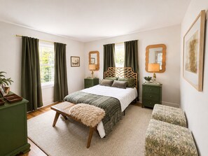 A bedroom with a bed, bedside tables, a bench, a chair, and a mirror.