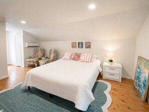 Ein Schlafzimmer mit einem Bett, zwei Nachttischen, einem Sessel, einem Teppich und Bildern an der Wand.